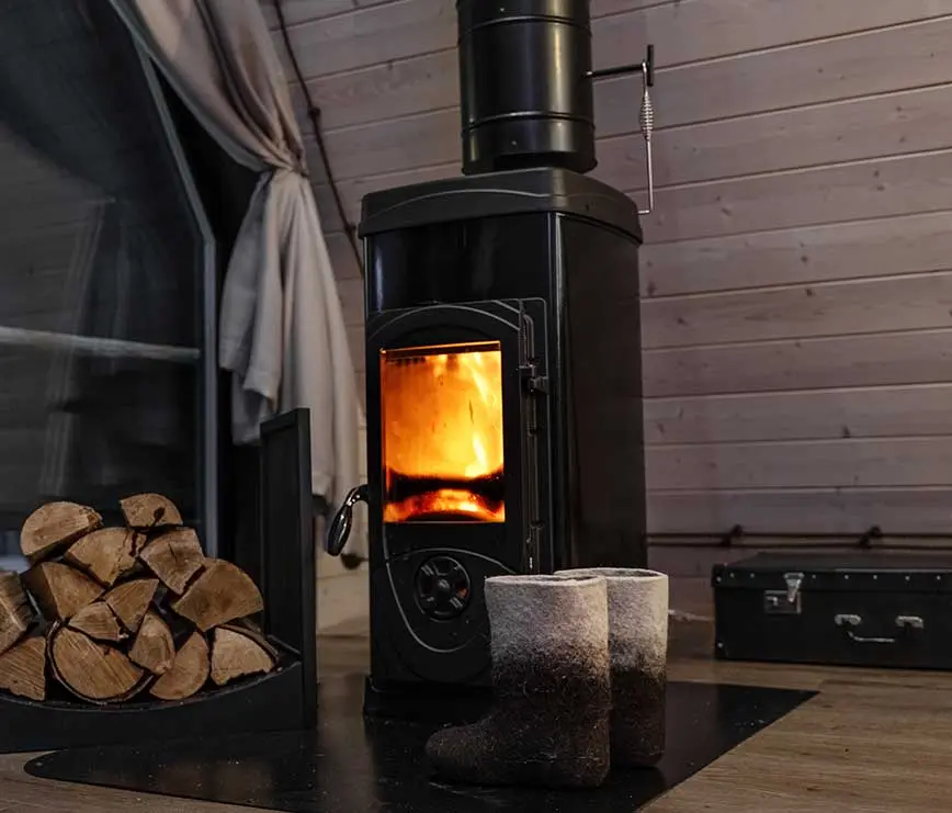 Holzofen mit Feuer und Holzvorrat in gemütlicher Hütte – Symbol für Wärme und Brandschutz.